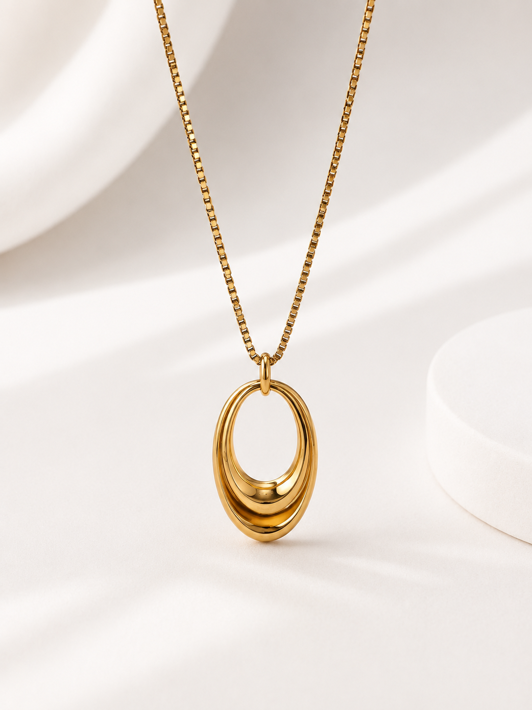 A gold chain necklace with a polished, multi-layered oval pendant, displayed on a clean white background with soft shadows.