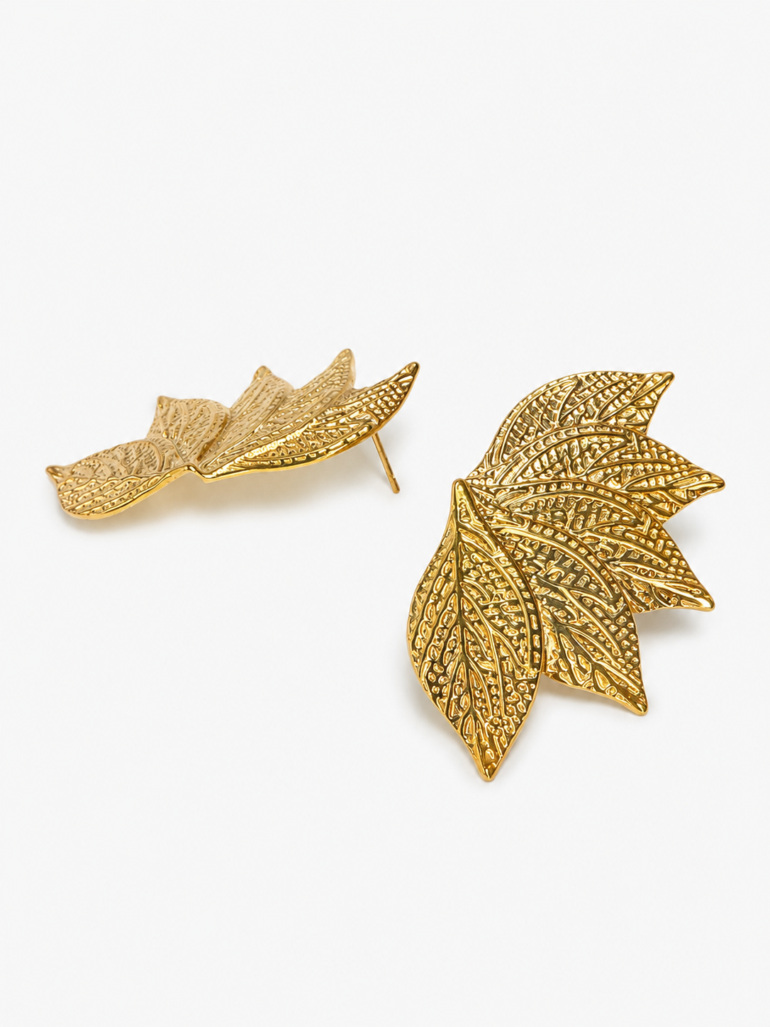 A pair of gold-toned leaf-shaped stud earrings with a textured, openwork leaf design, displayed on a clean white background.