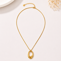 A gold chain necklace with a polished oval pendant, displayed on a light beige background with subtle decorative props.